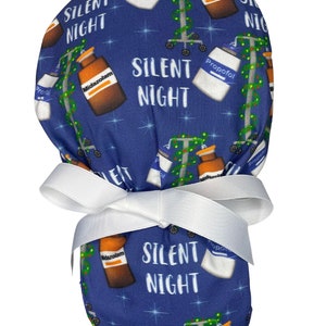May include: Blue scrub hat with a Christmas tree and medication bottle pattern. The hat has a white ribbon tied around it. The text "Silent Night" is repeated throughout the pattern.