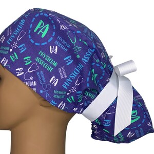 May include: Purple scrub hat with a white tie. The hat has a repeating pattern of the words "Physician Associate" and "PA" in green and blue text. A stethoscope symbol is also included in the pattern.