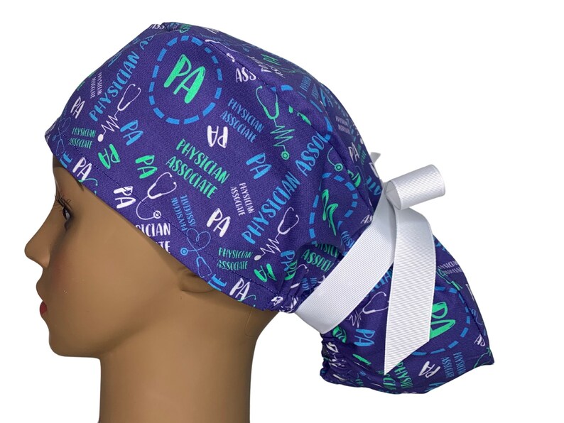 May include: Purple scrub hat with a white tie. The hat has a repeating pattern of the words "Physician Associate" and "PA" in green and blue text. A stethoscope symbol is also included in the pattern.