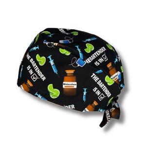 May include: Black surgical scrub cap with a repeating pattern of syringes, lime wedges, and medicine bottles. The text "THE BARTENDER IS IN" is printed on the cap.