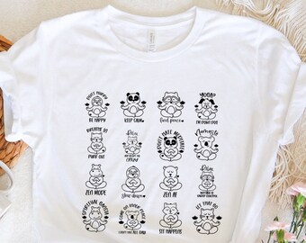 May include: White t-shirt with a black and white graphic design featuring a variety of animals in yoga poses. The text on the shirt includes phrases like "Don't Panic", "Be Happy", "Keep Calm", "Find Peace", "Yoga", "Namaste", "Zen Mode", "Zen AF", "Let That Go", "Sit Happens", and "Come Get Peace I Found You All Day".