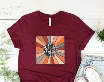 May include: Heather maroon short-sleeved t-shirt with a retro sunburst design and the text "Here Comes The Sun".