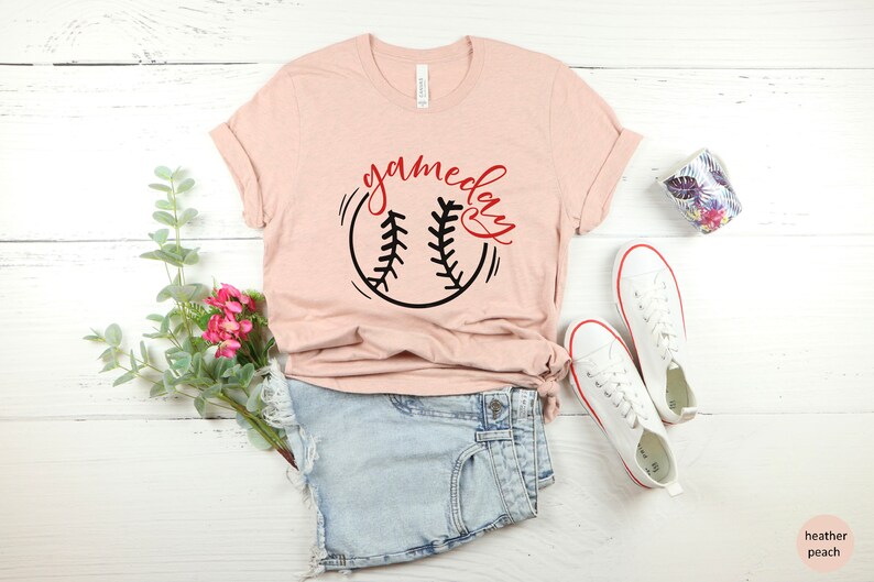 May include: A heather peach t-shirt with a black and white baseball graphic and the text "gameday" in red.