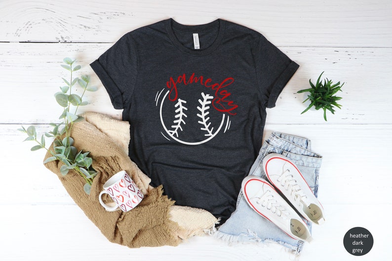 May include: Heather dark grey t-shirt with a white baseball graphic and the text "gameday" in red lettering.
