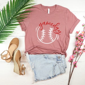 May include: A heather mauve t-shirt with a white baseball graphic and the text "game day" in red lettering.