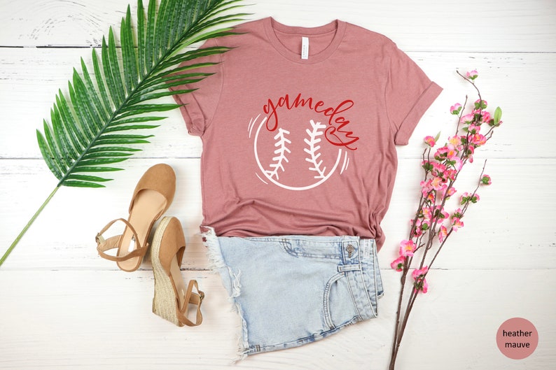 May include: A heather mauve t-shirt with a white baseball graphic and the text "game day" in red lettering.