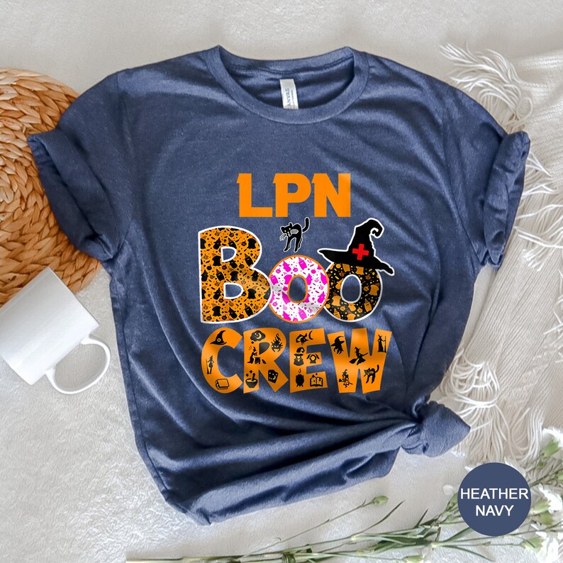 Pode incluir: Uma camiseta azul marinho com o texto "LPN BOO CREW" em letras laranja. O texto &eacute; cercado por &iacute;cones tem&aacute;ticos de Halloween, incluindo fantasmas, ab&oacute;boras, morcegos e bruxas.
