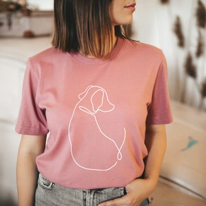 May include: A mauve t-shirt with a white line drawing of a dog on the front. The shirt is made of a soft, comfortable material.