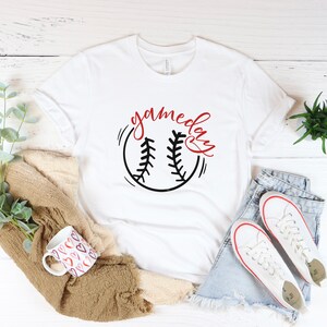 May include: White t-shirt with a black and red baseball graphic and the text "gameday" in red cursive lettering.