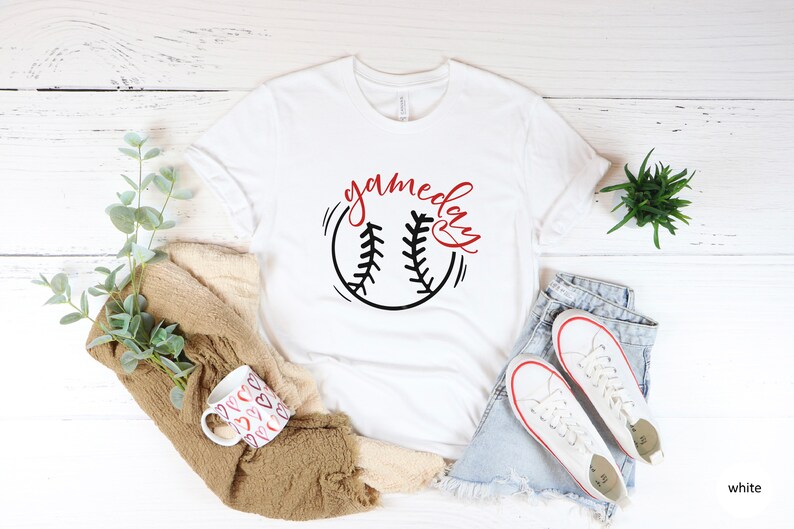 May include: White t-shirt with a black and red baseball graphic and the text "gameday" in red cursive lettering.