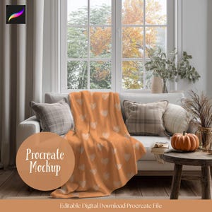 May include: An orange blanket with a white heart pattern draped over a white sofa. The scene includes decorative pillows, a small wooden table with a pumpkin, and a window with a view of fall foliage. The text "Procreate Mockup" is visible.