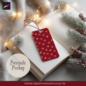 Può includere: Un segnalibro rosso con un motivo a cuori bianchi è appoggiato su un libro aperto. Il segnalibro è legato con uno spago rosso e bianco. Le parole "Procreate Mockup" sono visibili. L'immagine è decorata con luci di fata e verde.