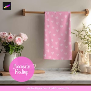May include: A pink kitchen towel with a pattern of white hearts hangs from a wooden rod. The towel is the focal point, with a vase of pink roses and a cutting board in the background. The words "Procreate Mockup" are in a pink circle.