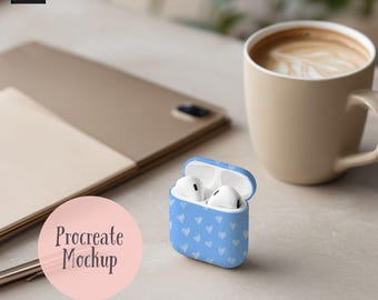 Könnte beinhalten: Hellblaues AirPod-Etui mit weißem Herzmuster, geöffnet, um weiße Ohrhörer zu zeigen. Eine beige Kaffeetasse und ein Tablet sind ebenfalls zu sehen. Die Worte "Procreate Mockup" stehen in einem rosa Kreis.