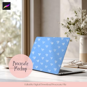 May include: A laptop with a light blue cover featuring a pattern of white hearts and small dots. The laptop is open on a white surface, with a coffee cup and a vase of white flowers in the background. The text "Procreate Mockup" is visible.