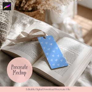 May include: An open book with a blue bookmark featuring a white heart pattern. A beige ribbon is placed on the pages. The text "Procreate Mockup" is in a pink circle. Below, the text reads "Editable Digital Download Procreate File."