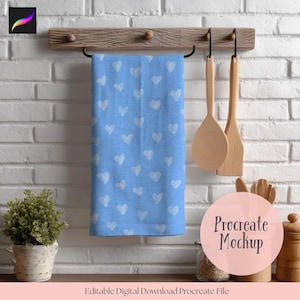 May include: A light blue kitchen towel with a white heart pattern hangs from a wooden rack. Two wooden cooking utensils hang to the right. A small potted plant and other kitchen items are visible.