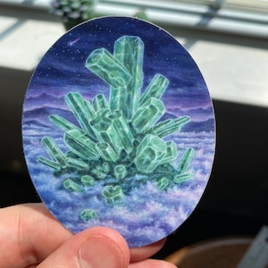 Puede incluir: Una formación de cristal verde, que se asemeja a una montaña, se representa sobre un fondo de cielo estrellado azul oscuro con un horizonte púrpura y rosa. El cristal está rodeado de nubes blancas.