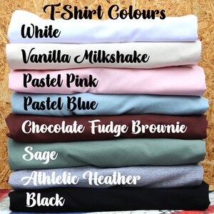 May include: A stack of folded t-shirts in various colors, including white, vanilla milkshake, pastel pink, pastel blue, chocolate fudge brownie, sage, athletic heather, and black. The text "T-Shirt Colours" is at the top of the image.