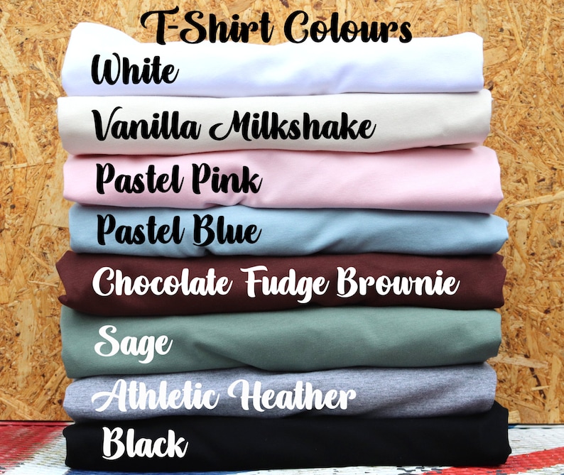 May include: A stack of folded t-shirts in various colors, including white, vanilla milkshake, pastel pink, pastel blue, chocolate fudge brownie, sage, athletic heather, and black. The text "T-Shirt Colours" is at the top of the image.