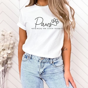 May include: White t-shirt with black text that reads "Paws and enjoy the little things" with a paw print graphic.