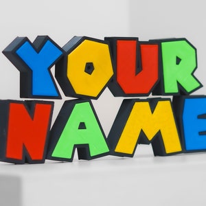 Puede incluir: Un letrero de letras de bloque de colores que dice "YOUR NAME" en negro, rojo, amarillo, verde y azul.