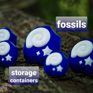 May include: Blue and white fossil-shaped storage containers with the word "fossils" printed on a white label. The containers are on a wooden surface.