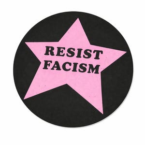 May include: A circular black sticker featuring a pink star with the words "RESIST FACISM" in bold, black text. The sticker's design is simple and bold, likely made of paper or a similar material.
