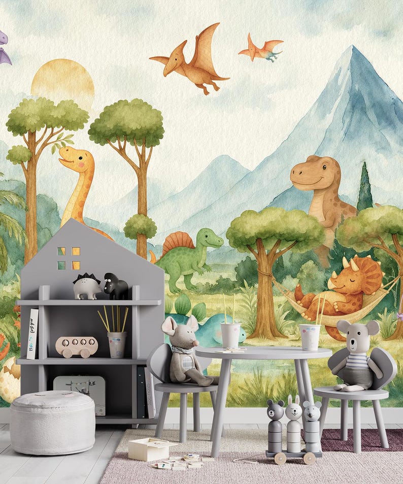 May include: A children's playroom scene with a dinosaur theme. The image shows a gray bookshelf, table, and chairs, decorated with soft toys and ornaments. The backdrop is a mural depicting dinosaurs, trees, mountains, and pterodactyls in watercolour.