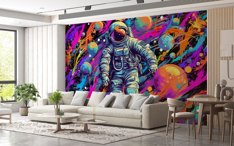 May include: An astronaut in a blue and white spacesuit floats in a colorful galaxy with planets and stars. The background is a dark blue with splashes of pink, purple, yellow, and orange paint.