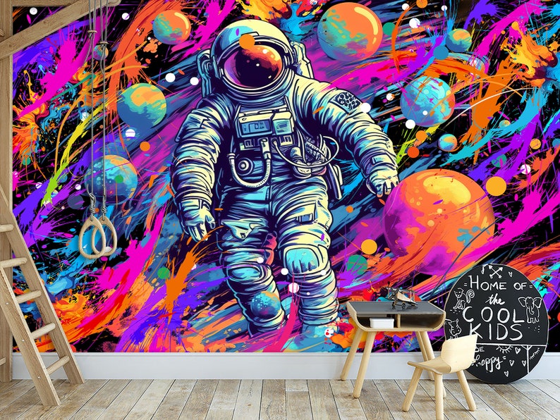 May include: A colorful astronaut illustration with a black background and splashes of paint in pink, blue, orange, and yellow. The astronaut is wearing a white spacesuit with a blue helmet and is surrounded by planets. The text "Home of the Cool Kids" is written on a black circle.