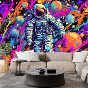 May include: A colorful abstract space scene with a blue astronaut floating in front of a large orange planet. The background is filled with splashes of pink, purple, yellow, and blue paint.