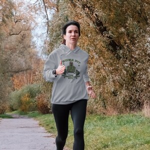 May include: A person running on a path wearing a grey hoodie with the text "BOBA FIT" and a graphic of a character with a barbell. The hoodie also has the text "THE MANDALORIAN GYM". The person is wearing black leggings and a watch.