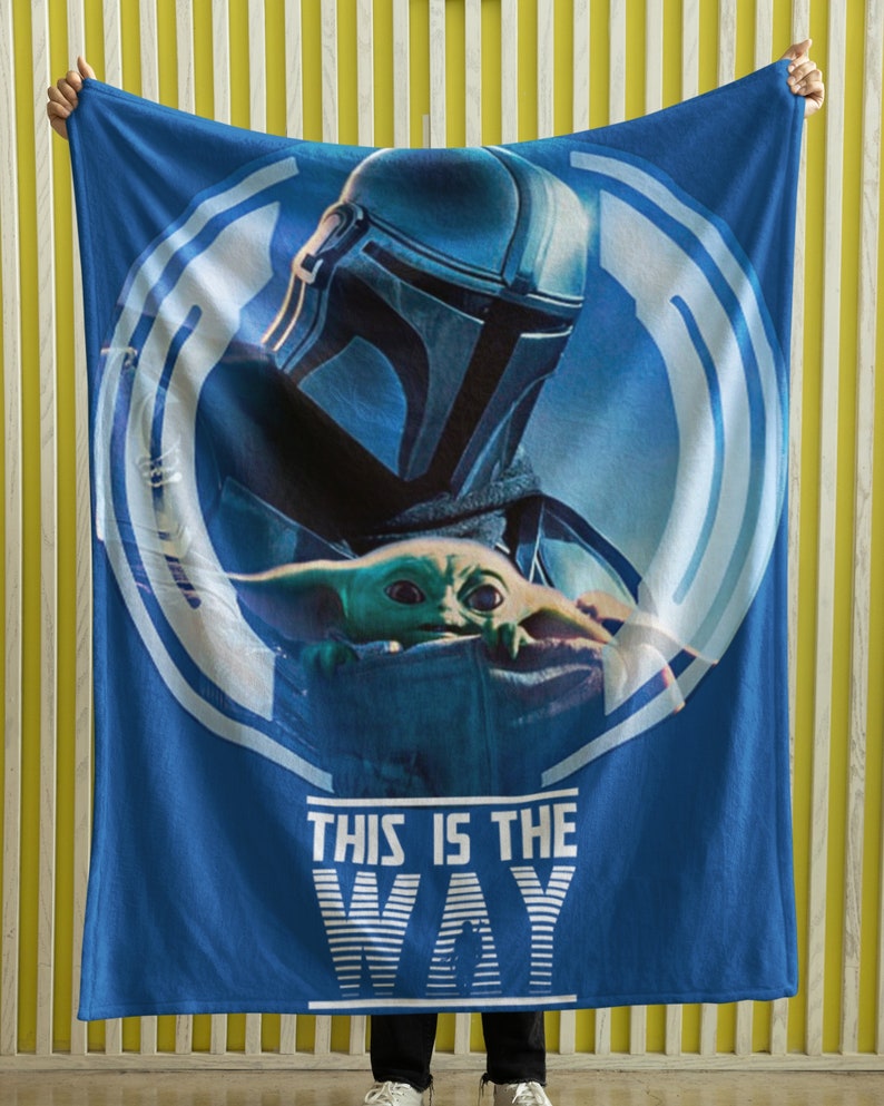 May include: Blue fleece blanket with a white circle design featuring a Mandalorian and Grogu. The text "This is the Way" is printed in white below the circle.