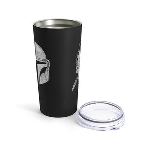 Puede incluir: Una taza de viaje de acero inoxidable negro con un contorno blanco de un casco mandaloriano y una figura con un jetpack en un lado. La taza tiene una tapa transparente.