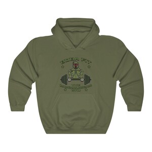 May include: Khaki green hooded sweatshirt with a front graphic. The graphic shows a cartoon Mandalorian character lifting weights, with the text "BOBA FIT THE MANDALORIAN GYM". The sweatshirt has a kangaroo pocket and a drawstring hood.