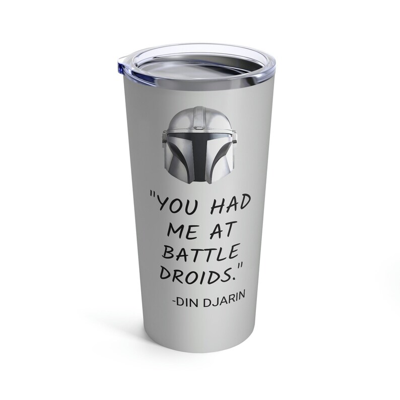 May include: A stainless steel tumbler with a gray background featuring a black and white illustration of a Mandalorian helmet. The text "You had me at battle droids." is printed below the helmet, with the text "Din Djarin" printed below that.