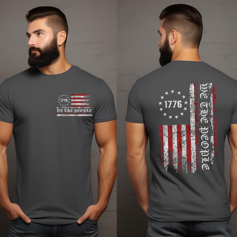 May include: A dark grey t-shirt with a distressed American flag design. The flag has red and white stripes and a blue field with white stars. The text "1776" and "We the People" is printed in white on the shirt.