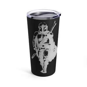 Puede incluir: Un vaso de acero inoxidable negro con una silueta blanca de un personaje mandaloriano sosteniendo un arma. El personaje lleva un casco y una armadura.