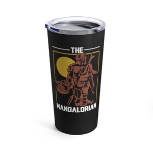 Op de afbeelding: Een zwarte roestvrijstalen tumbler met een afbeelding van The Mandalorian en Grogu. De afbeelding is in een geel en oranje kleurenschema met de tekst "THE MANDALORIAN".