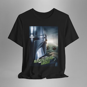 May include: Black t-shirt featuring a graphic from The Mandalorian series. The design includes the Mandalorian's helmet and Grogu, with the text "The Mandalorian and Grogu" in green and white.