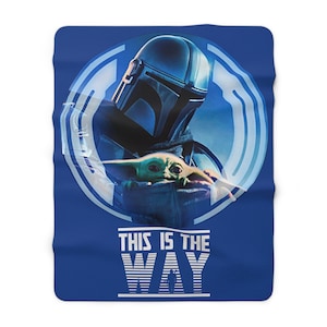 May include: A blue throw blanket with a white circle featuring a blue and white Mandalorian character holding a small green alien. The text "This is the Way" is printed in white below the circle.