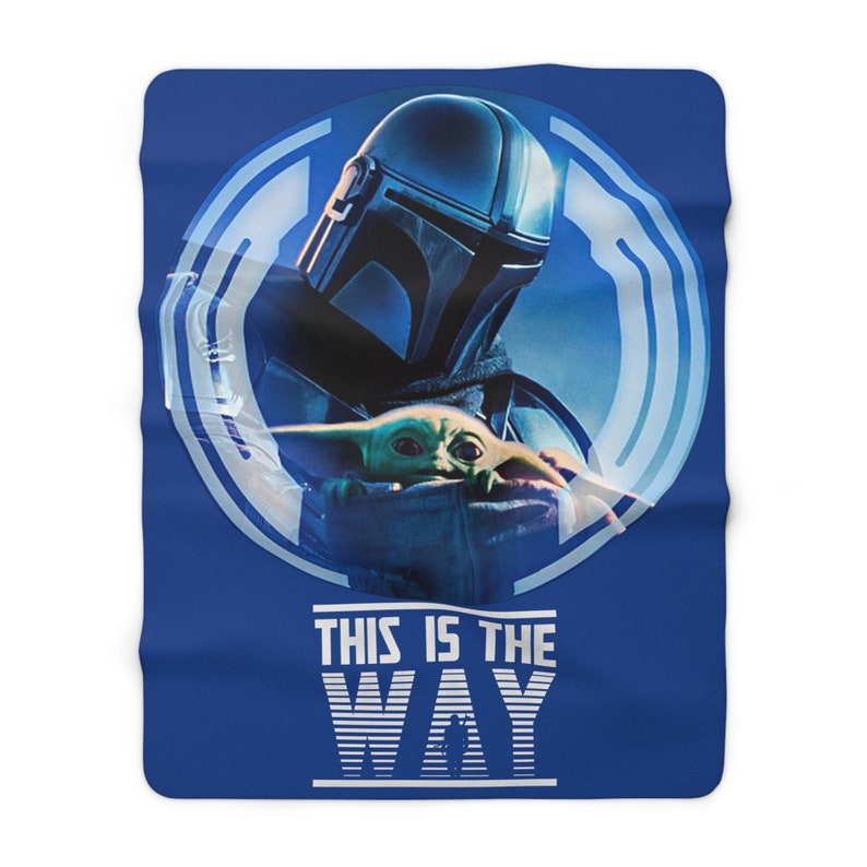 May include: A blue throw blanket with a white circle featuring a blue and white Mandalorian character holding a small green alien. The text "This is the Way" is printed in white below the circle.
