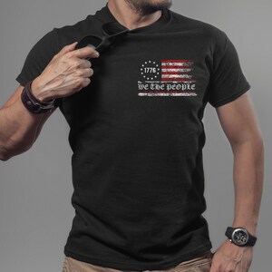 May include: Black t-shirt featuring a distressed American flag design with the text "1776 We the People".