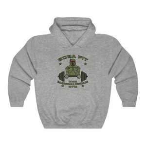 May include: A grey hooded sweatshirt featuring the text "BOBA FIT THE MANDALORIAN GYM" and a green and brown graphic of a character lifting weights. The sweatshirt is made of a soft material and is suitable for casual wear.