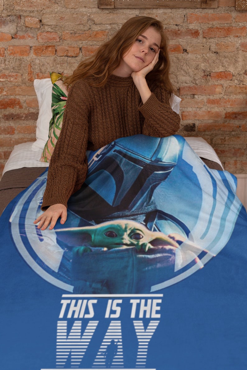 May include: A blue throw blanket with a graphic of a Mandalorian character holding a small green alien. The text "This is the Way" is printed in white on the blanket.
