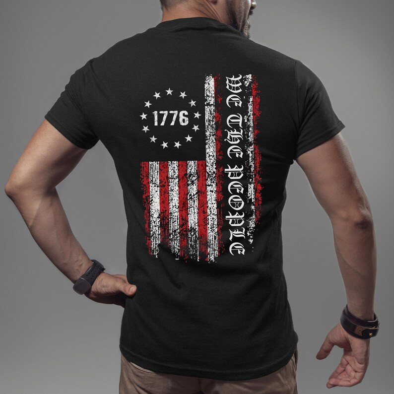May include: Black t-shirt featuring a distressed American flag design with the text "We The People" and "1776" printed on the back.