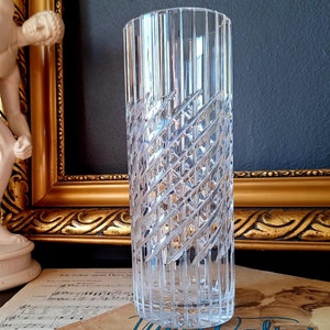 Könnte beinhalten: Eine klare Glasvase mit Diamantenmuster steht auf einem Blatt Musik. Die Vase ist hoch und zylindrisch. Die Musik ist für ein Klavierstück namens "Nure Walzer von Frau".