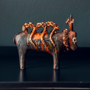 Op de afbeelding: Een keramiek stierenbeeldje met een bruine en oranje glazuur. De stier is versierd met kleine, bloemvormige figuren op zijn rug.