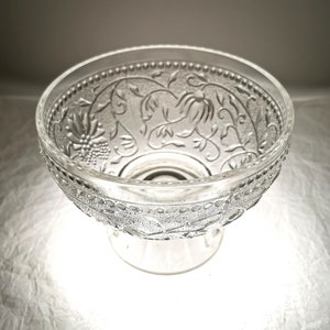 May include: A clear glass bowl with an intricate floral design. The bowl has a pedestal base and is perfect for serving snacks or desserts.